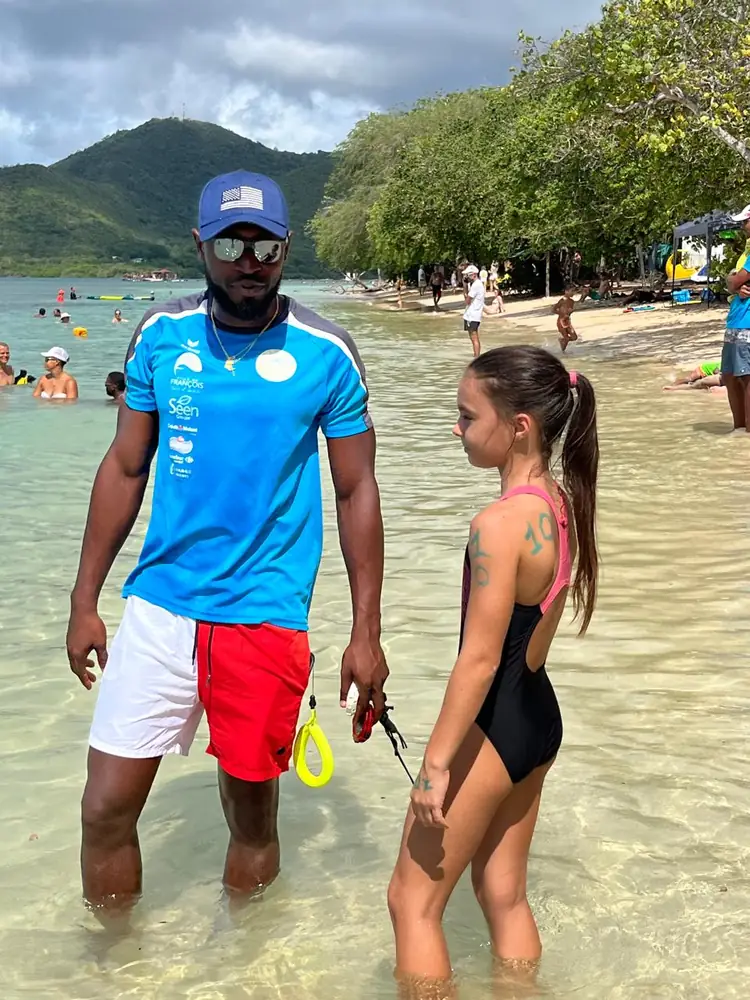 Un entraîneur du FNC et une jeune nageuse dans l'eau au bord de la plage, derniers conseils avant le départ
