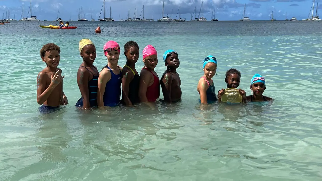 Les jeunes nageurs du FNC alignés dans l'eau à la Pointe Marin avant le départ, voiliers au mouillage en arrière-plan