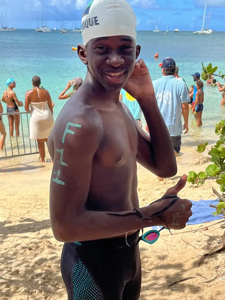 Un nageur en bonnet de la Martinique, numéro F11 tracé sur l'épaule, pouce levé sur la plage avant le départ