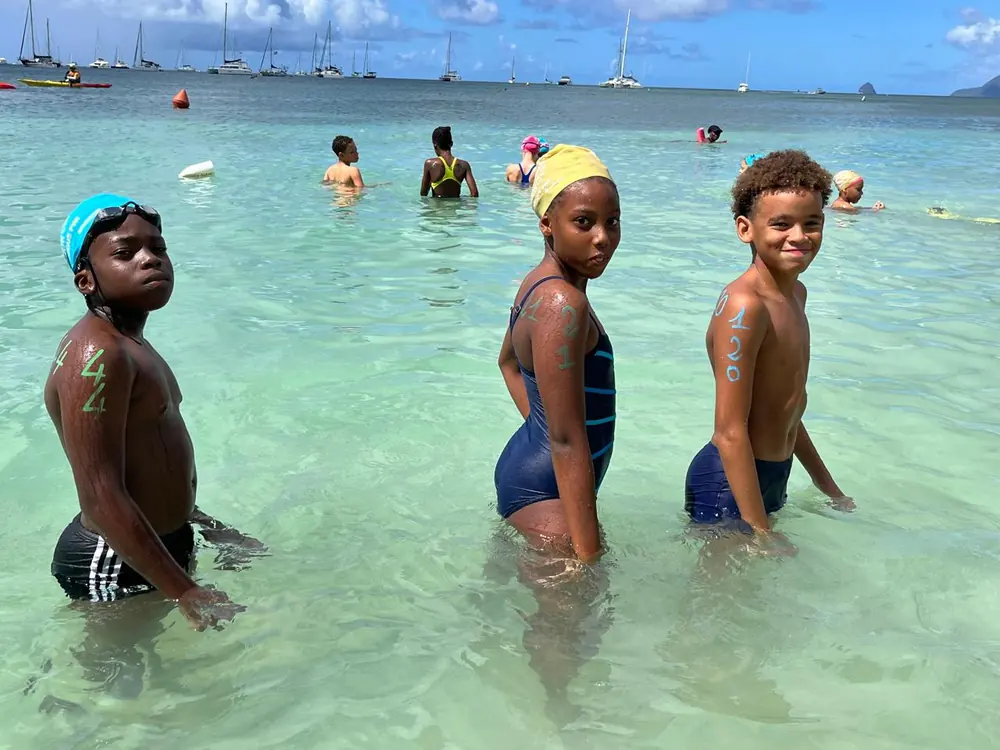 Trois jeunes nageurs dans l'eau montrent leur numéro de course tracé sur l'épaule