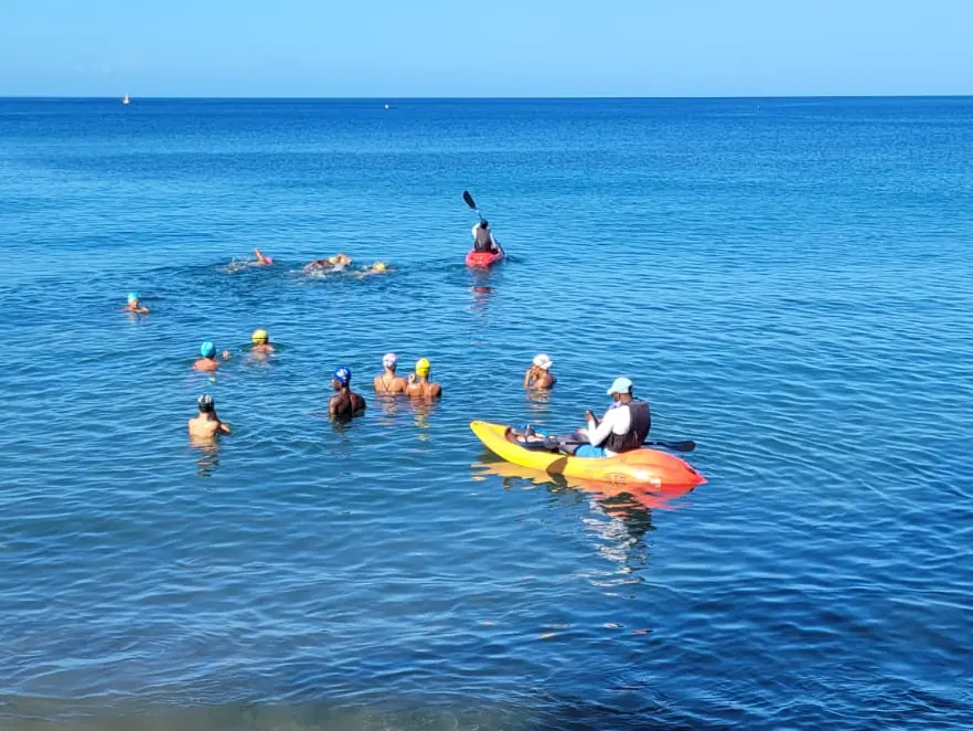 Un kayak orange escorte un groupe de nageurs au large