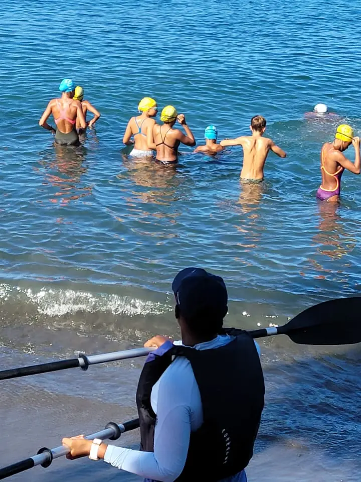 Une kayakiste en gilet de sauvetage, pagaie en main, au bord de l'eau pendant que les nageurs entrent dans la mer