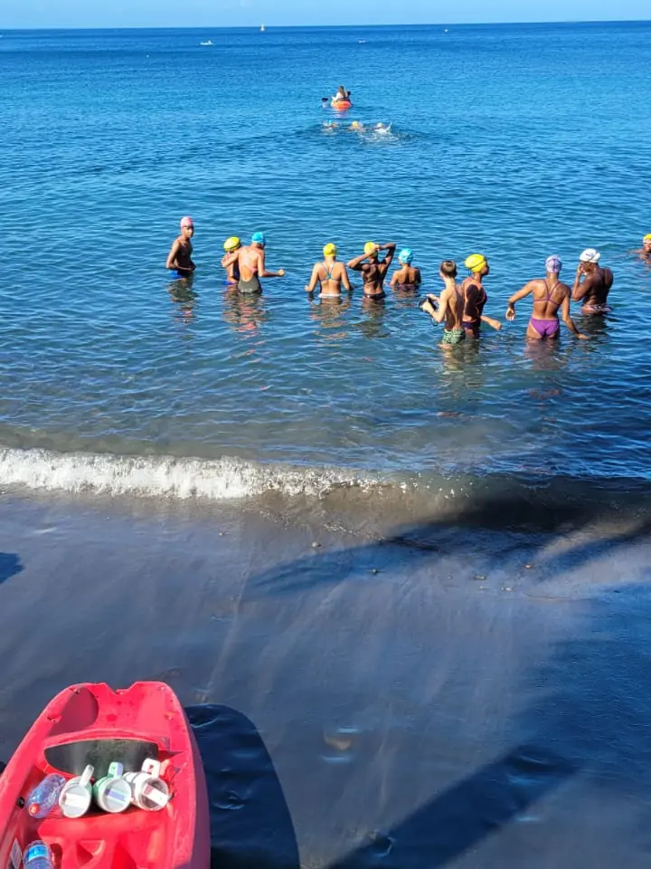 Un kayak rouge chargé de bouteilles d'eau sur la plage, les nageurs partent vers le large
